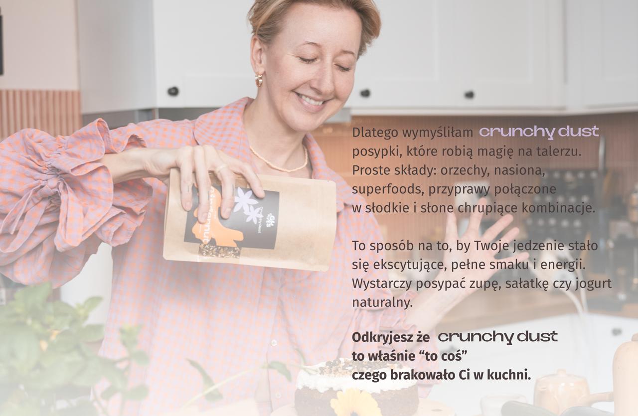 Ania posypuje ciasto posypką Crunchy Dusty GingerNut. Napis: Dlatego wymyśliłam Crunchy Dust – posypki, które robią magię na talerzu. Proste składy: orzechy, nasiona, superfoods, przyprawy połączone w słodkie i słone chrupiące kombinacje. To sposób na to, by Twoje jedzenie stało się ekscytujące, pełne smaku i energii. Wystarczy posypać zupę, sałatkę czy jogurt naturalny. Odkryjesz że Crunchy Dust to właśnie “to coś” czego brakowało Ci w kuchni.