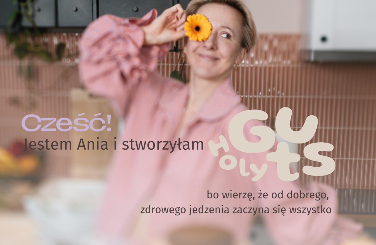 Ania z kwiatem w kuchni. Napis: Cześć, jestem Ania i stworzyłam Holy Guts, bo wierzę, że od dobrego, zdrowego jedzenia zaczyna się wszystko. 